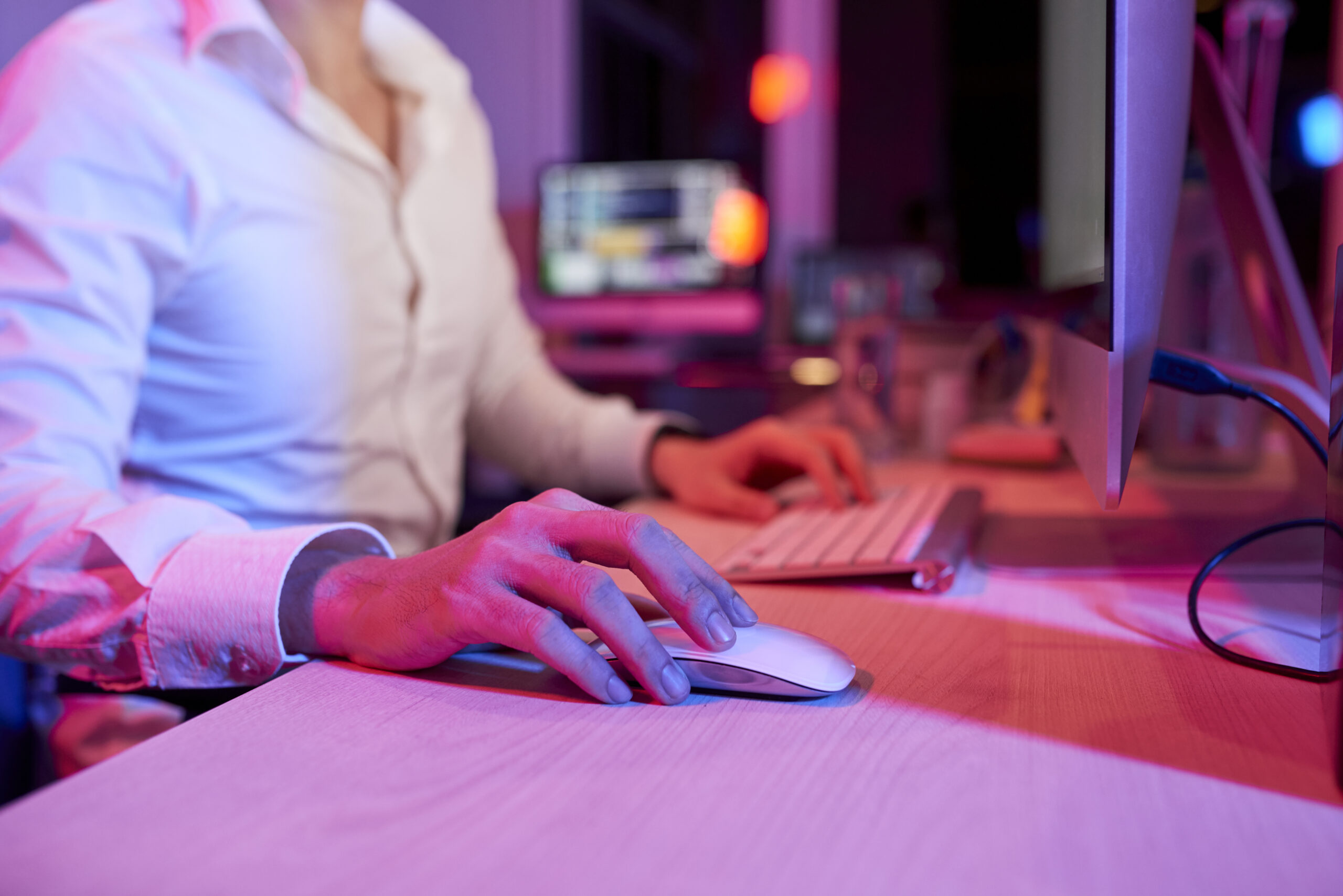 Close-up image of entrepreneur using computer mouse when working at office desk at night, pink light